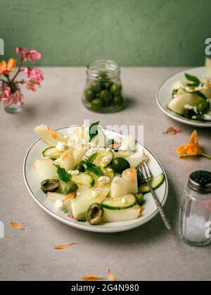 Köstlicher Melonensalat mit Gurken und Oliven auf Teller mit Kräutern in der Nähe von Salzstreuer und Serviette serviert Stockfoto