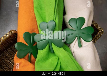 Nahaufnahme von St. Patricks Day Kleeblatt Serviettenhalter auf hell Orange grüne und weiße Stoffservietten in goldenem Korb Stockfoto