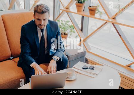 In der Lobby sitzt ein erfolgreicher, gepflegter Finanzier in einem stilvollen Anzug mit beschnittenem Bart Stockfoto