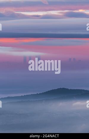 Luftaufnahme der modernen Wolkenkratzer von Cuatro Torres in madrid und der Berge, die von Zeckenwolken bedeckt sind, unter dem farbenfrohen Himmel während des Sonnenaufgangs Stockfoto