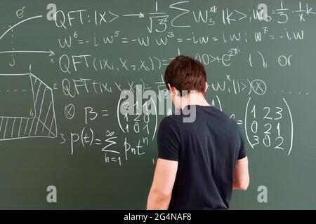 Männliche Person, die Text mit einem Stück Kreide auf der Tafel schreibt, indem sie mathematische und physikalische Gleichungen macht Stockfoto