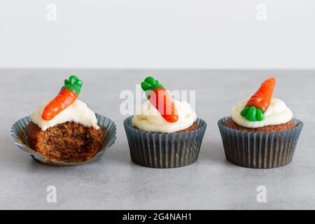 Reihen von süßen, köstlichen Karotten-Cupcakes mit zartem Creme und karottenförmigen Gummitüffeln auf grauer Oberfläche Stockfoto