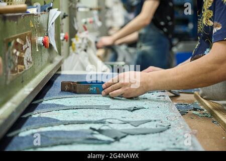 Detail des Arbeiters, der das Schnittmuster beim Schneiden von Stoff in der chinesischen Schuhfabrik verwendet Stockfoto