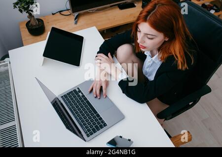 Von oben junge Unternehmerin, die am Schreibtisch mit Tablet und Smartphone zu Hause am Netbook arbeitet Stockfoto