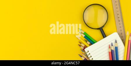Back to School und Education Concept Banner mit Notizblock, Farbstiften und Lupe auf dem gelben Tisch, Draufsicht und Kopierraum Stockfoto