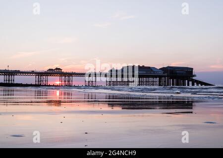 Sonnenuntergang hinter dem Cromer Pier an der North Norfolk Küste, aufgenommen im Juni 2021 vom East Beach bei Ebbe. Stockfoto