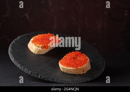 Sandwiches mit rotem Kaviar auf einem schwarzen Tablett mit Kaviar-Sandwiches. Rot und schwarz. Stockfoto
