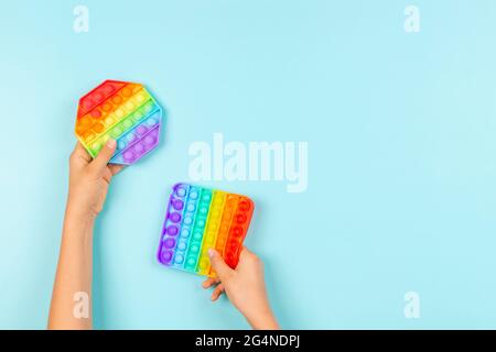 Kinder Hände halten bunte Pop it fidget Spielzeug auf blauem Hintergrund. Push Pop-it zappelnde Spiel für Kinder Stockfoto