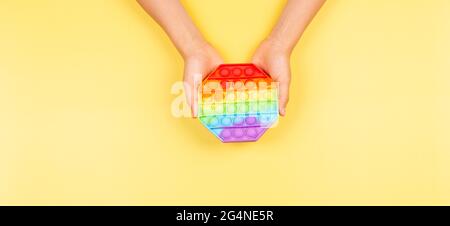 Kind Hand hält Pop it Fidget Spielzeug auf gelbem Hintergrund. Push Pop-it zappelnde Spiel hilft Stress, Angst zu lindern Stockfoto