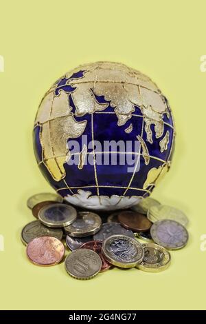Globale Wirtschaft - schöner emaillierter Weltglobus auf einem Haufen Münzen aus aller Welt auf gelbem Hintergrund - selektiver Fokus Stockfoto
