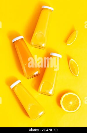 Orangensaft in Flaschen und Orangen auf gelbem Hintergrund. Das Konzept eines saftigen, hellen Sommers Stockfoto