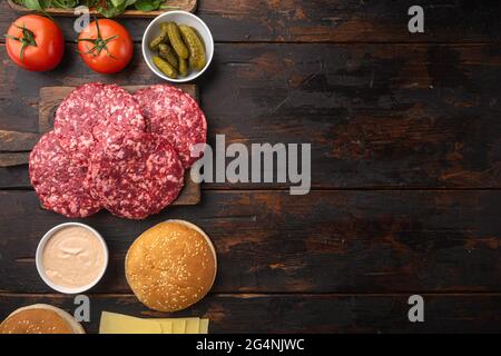 Zutaten zum Kochen von Burgern. Hackfleisch-Hacksteaks, Brötchen, Tomaten, Kräuter und Gewürze Set, auf altem dunklen Holztisch Hintergrund, Draufsicht flach liegend, wi Stockfoto