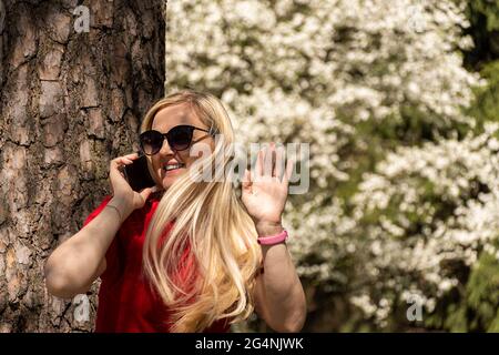 Hübsche junge Frau, die draußen in einem Park auf dem Smartphone spricht Stockfoto