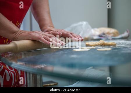 Frau rollt Teig zum Kochen auf dem Tisch in der Küche. Stockfoto