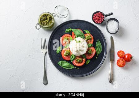 Buffalo Burrata Käse serviert mit frischen Tomaten und Basilikumblättern Pesto-Sauce auf schwarzem Teller weißen Hintergrund Platz für Text. Stockfoto