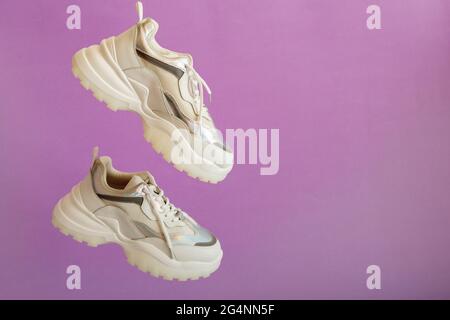 Städtische weiße Neon Sneakers fliegen auf farbigem violettem Hintergrund mit Kopierraum. Weiße Sport Sneakers Schuhe Levitation. Paar sportliche weibliche Sneakers. Stockfoto