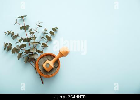 Eukalyptuszweige und Holzmörtel auf farbigem blauem Hintergrund mit Kopierraum. Eukalyptus pflanzliche Apotheker Heilkräuter für homöopathische Stockfoto