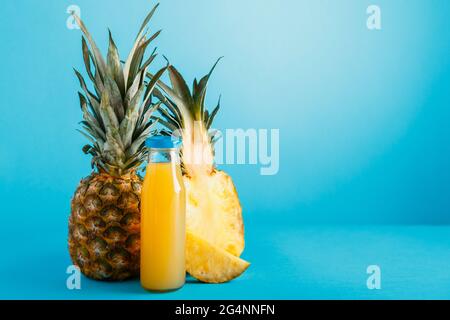 Leckerer Ananassaft in Glasflasche mit Zutaten auf blauem Sommerhintergrund mit Kopierraum. Frischer natürlicher Ananascocktail, Ananas Stockfoto