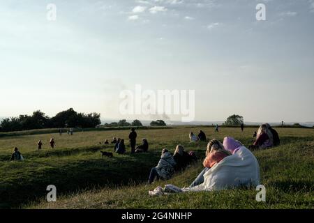 Gruppen von Menschen sitzen und warten auf den Sonnenuntergang an der Sommersonnenwende, dem längsten Tag des Jahres.Menschen kommen seit 6,000 Jahren an diesen Ort, um die landschaftliche Aussicht zu genießen und die alte und spirituelle Tradition zu praktizieren. Eine große Anzahl von Zuschauern, jung und alt, viele begleitet von Hunden, versammelten sich auf dem Hügel von Tara in der Grafschaft Meath, um den Sonnenuntergang an der Sommersonnenwende am 21. Juni zu sehen. Der Hügel von Tara ist ein neolithisches Durchgangsgrab und eine Stätte von wichtiger historischer Bedeutung in der irischen Folklore. Eine große Anzahl von Zuschauern, jung und alt, viele begleiteten wi Stockfoto