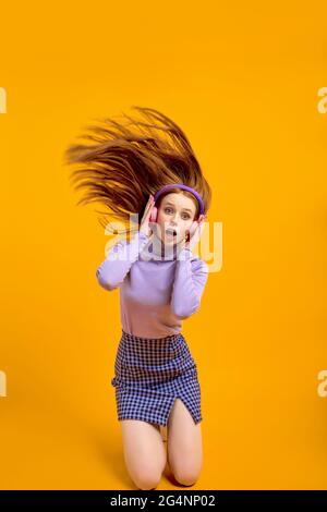 Emotionale junge glücklich verrückte Frau in Kopfhörer mit fliegenden Haaren isoliert auf gelbem Hintergrund im Studio, Porträt. Aufgeregter kaukasischer weiblicher Witz Stockfoto