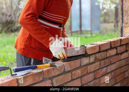 Ein Mann baut eine Ziegelmauer, legt einen Ziegel auf einen Zement-Sand-Mörtel Stockfoto