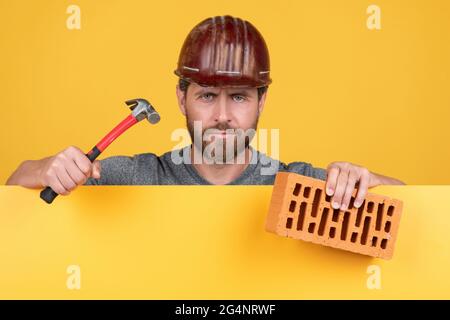 Maurer. Reifer Mann im Helm mit Hammer und Ziegel. baumeister bärtiger Arbeiter Stockfoto