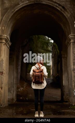 Rückansicht auf Reisende Frau mit Rucksack stehen in historischen alten Bogen, erkunden interessante alte Stätten und Attraktionen, historische Orte, an aut Stockfoto