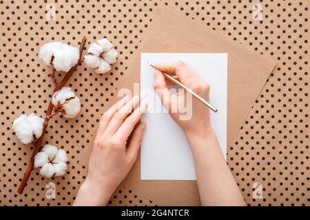 Weibliche Hände schreiben Brief auf Tisch mit Baumwolle blühenden Blumen. Frau machen Wunschliste oder Liste flach legen zu tun. Mädchen schreibt Schild Grußkarte. Stockfoto