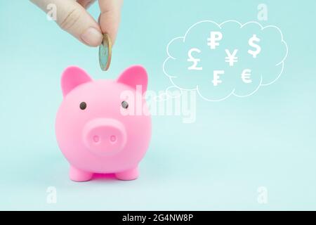 Hand, die eine Münze in Sparschwein mit digitalen Hologramm Weltwährungen in Wolke dachte über seinem Kopf auf blauem Hintergrund. Globaler Währungswechsel Stockfoto