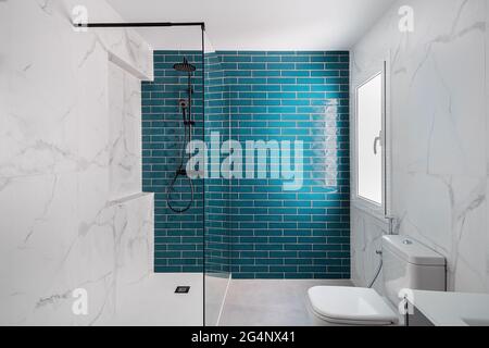 Dekoriert mit dunklem Aquamarin und weißen Farben. Modernes gefliestes Badezimmer mit Duschzone, neuem Waschbecken und Toilette. Stockfoto