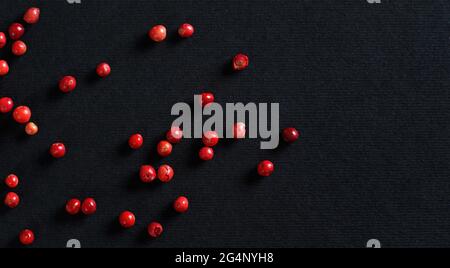 Ganze rosa / rote Pfefferkörner auf schwarzem / grauem Papier, Ansicht von oben, Platz für Text rechts Stockfoto