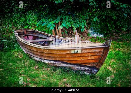 Altes hölzernes Ruderboot, das am Rand eines Teiches auf einer Wiese verlassene liegt. Stockfoto