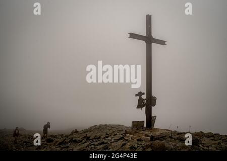 Zwei Wanderer kommen inmitten des Nebels am Kreuz an, das den Gipfel des Puigmal-Berges auf 2914 Metern (9560 Fuß) in den katalanischen Pyrenäen markiert. Stockfoto