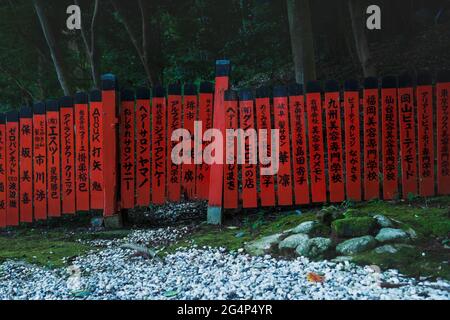Roter Zaun mit japanischem Text entlang Wald und moosbedeckten Steinen am Mikami-jinja-Schrein in Kyoto, Japan Stockfoto