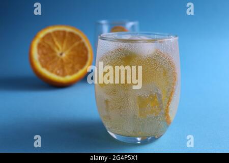 Schritt-für-Schritt-Herstellung von Limonade. Schritt 2. Gießen Sie die Fruchtorange mit Sodawasser. Ein Glas Limonade orange auf blauem Hintergrund mit Platz für Text Stockfoto