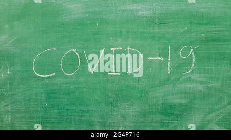 Covid-19 Wort geschrieben auf grüner Tafel mit weißer Kreide im Klassenzimmer Stockfoto