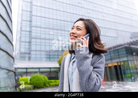 Junge schöne Mädchen zu Fuß außerhalb Bürogebäude mit Handy und glücklich Kunden anrufen Stockfoto