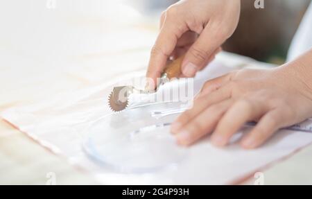 Nahaufnahme der Schneidertisch mit weiblichen Händen zeichnen Stoff mit Kurve Lineal für die Herstellung eines Musters für Kleidung in Werkstatt-Studio. Stockfoto