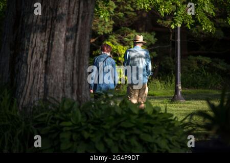 Ein älteres Paar, das in einem öffentlichen Park mit dichtem Grün spazierengeht. Stockfoto