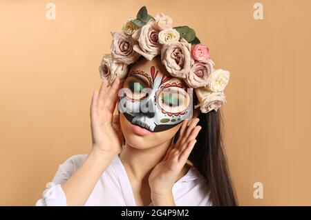 Junge Frau mit malte Schädel auf ihrem Gesicht des mexikanischen Tag der Toten gegen Farbe Hintergrund Stockfoto