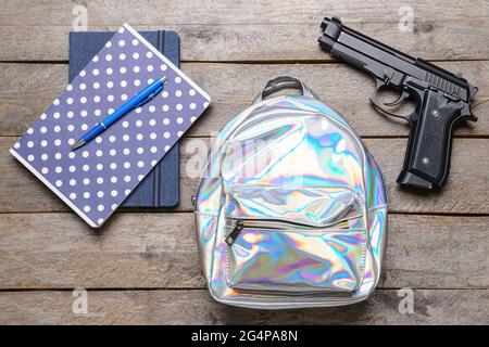 Pistole und Rucksack mit Papeterie auf Holzhintergrund. Konzept des Schussdrehens Stockfoto