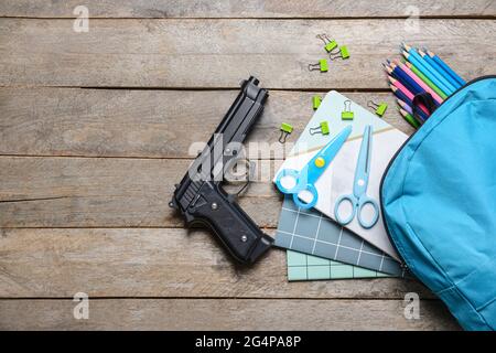 Pistole und Rucksack mit Papeterie auf Holzhintergrund. Konzept des Schussdrehens Stockfoto