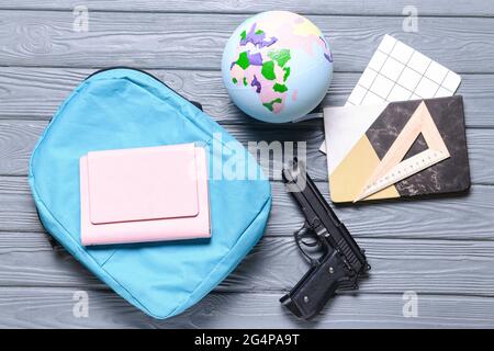 Pistole und Rucksack mit Papeterie auf Holzhintergrund. Konzept des Schussdrehens Stockfoto