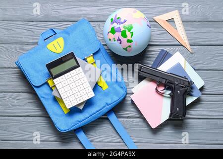 Pistole und Rucksack mit Papeterie auf Holzhintergrund. Konzept des Schussdrehens Stockfoto