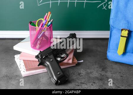 Pistole und Schreibwaren auf dem Tisch im Klassenzimmer. Konzept des Schussdrehens Stockfoto