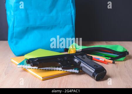 Pistole und Schreibwaren auf dem Tisch im Klassenzimmer. Konzept des Schussdrehens Stockfoto