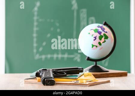 Pistole und Schreibwaren auf dem Tisch im Klassenzimmer. Konzept des Schussdrehens Stockfoto