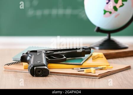 Pistole und Schreibwaren auf dem Tisch im Klassenzimmer. Konzept des Schussdrehens Stockfoto