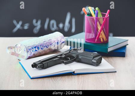 Pistole und Schreibwaren auf dem Tisch im Klassenzimmer. Konzept des Schussdrehens Stockfoto