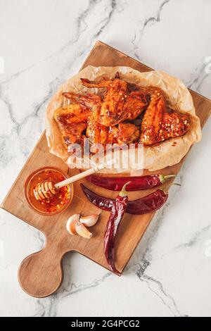 Schüssel mit heißem Honig, trockener Chilischote, Knoblauch und gebratenen Hähnchenflügeln auf hellem Hintergrund Stockfoto